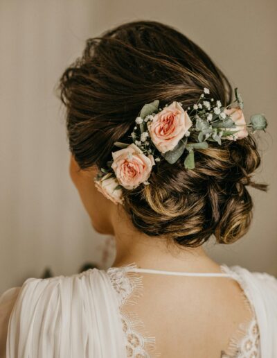 "Femme de dos avec un chignon bas de mariée travaillé, coiffure de fête chic avec mèches naturelles."